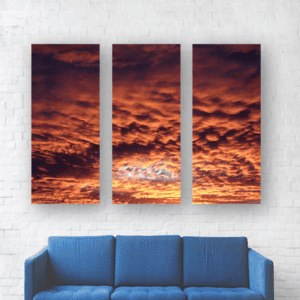 Cielo al atardecer con nubes rojas y naranjas en un mural de tres cuadros en pared blanca.