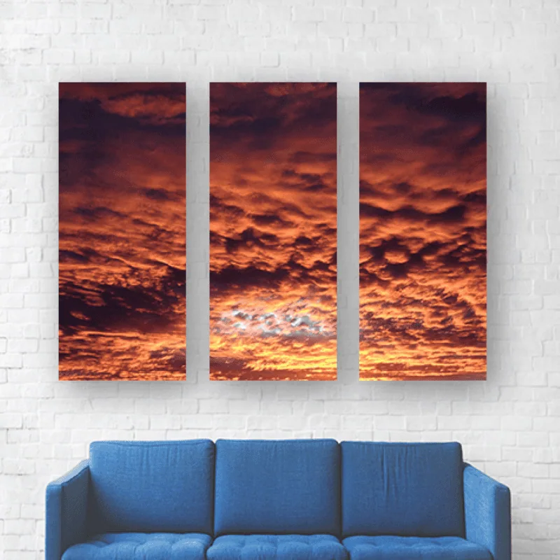 Cielo al atardecer con nubes rojas y naranjas en un mural de tres cuadros en pared blanca.